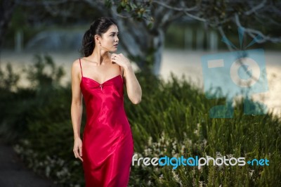 Beautiful Young Woman In The Gardens Wearing A Long Silk Red Dress Stock Photo