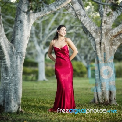 Beautiful Young Woman In The Gardens Wearing A Long Silk Red Dress Stock Photo