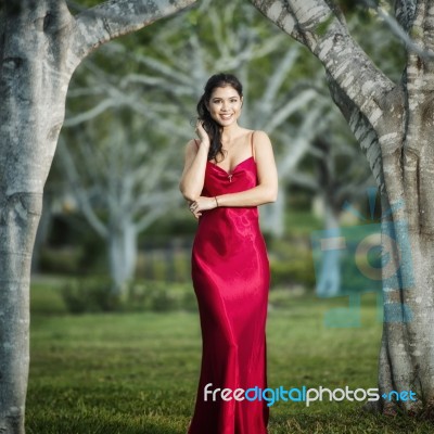 Beautiful Young Woman In The Gardens Wearing A Long Silk Red Dress Stock Photo