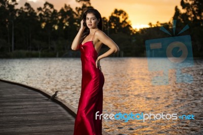 Beautiful Young Woman In The Gardens Wearing A Long Silk Red Dress Stock Photo