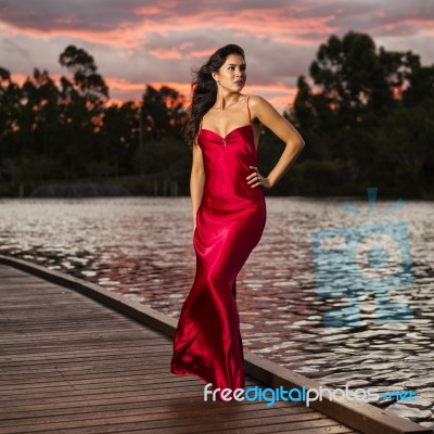 Beautiful Young Woman In The Gardens Wearing A Long Silk Red Dress Stock Photo