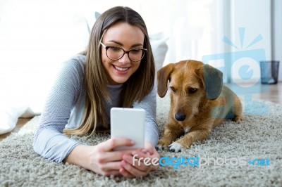 Beautiful Young Woman With Her Dog Using Mobile Phone At Home Stock Photo