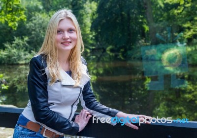 Blond Girl Leaning On Fence Near Water In Forest Stock Photo