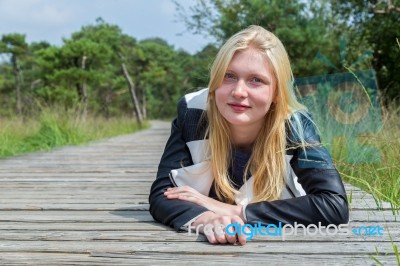 Blonde Girl Lying On Wooden Path In Nature Stock Photo