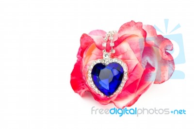 Blue Jewelry Heart Hanging In Red Rose Stock Photo