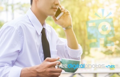 Business Man Using Mobile Phone And Hold A Cup While Sitting In Stock Photo