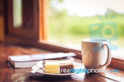 Cake And Cup Of Coffee On Wooden Table Near Window Sill. Time With Snacks Concept Stock Photo