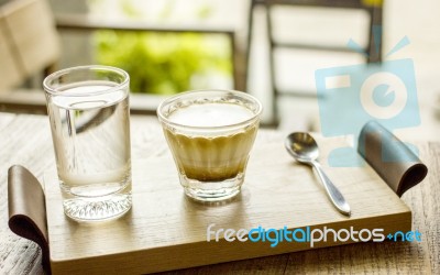 Cappuccino Coffee Cup With Glass Of Water Serving On Wooden Tray On Coffee Table Stock Photo