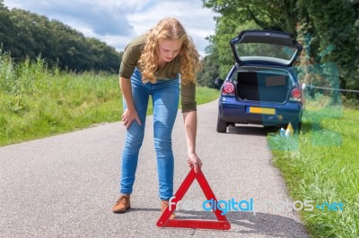 Caucasian Woman Placing Warning Triangle On Rural Road Stock Photo