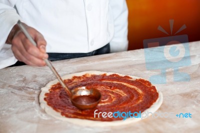 Chef Baker Spreading Sauce On Pizza Base Stock Photo