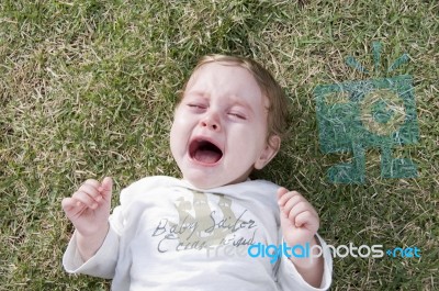 Child Crying And Lying On Grass Stock Photo