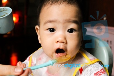 Close Up Of Happy Little Seven Months Old Son In See Through Plastic Bib Eating In Chair For Babies After Mom Made Him Eat Avocado And Banana Mix.happy Baby's Face. Asian Infant Open Mouth Stock Photo