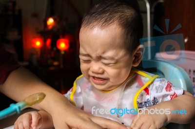 Close Up Of Unhappy Little Seven Months Old Son In See Through Plastic Bib Screaming And Crying In Chair For Babies After Mom Made Him Eat Avocado And Banana Mix.unhappy Baby's Face. Asian Infant Cry Stock Photo