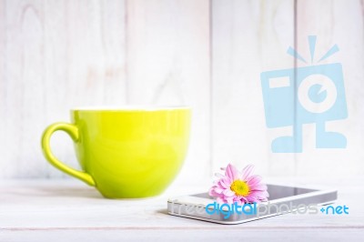 Coffee Cup And A Mobile Phone With Flowers On The White Wooden Stock Photo