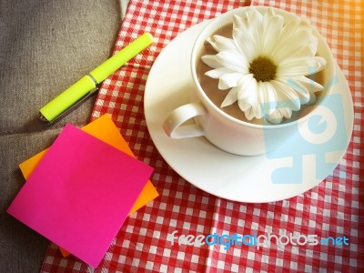 Coffee Cup On Table With White Daisy And Sticky Note, Pen Stock Photo