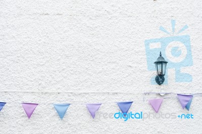 Colorful Party Flags Bunting Hanging On White Wall Background With Wall Lamp Light. Minimal Hipster Style Design Stock Photo