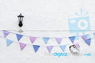 Colorful Party Flags Bunting Hanging On White Wall Background With Wall Lamp Light. Minimal Hipster Style Design Stock Photo