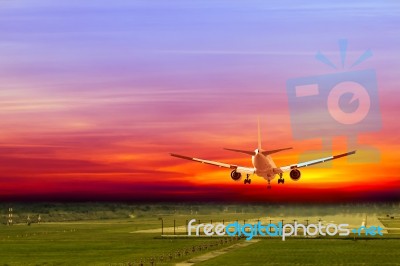 Commercial Airplane Landing On Runway In Airport At Sunset Stock Photo