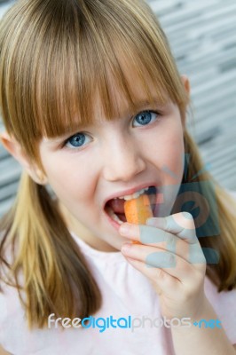 Cute Little Girl Eats Carrot And Looking At The Camera Stock Photo