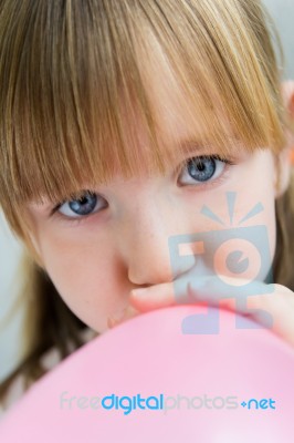 Cute Little  Girl Inflating A Pink Balloon In The Kitchen Stock Photo