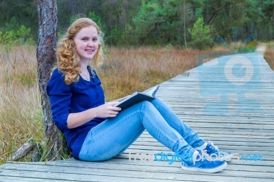 Dutch Girl Reading Book On Wooden Path In Forest Stock Photo