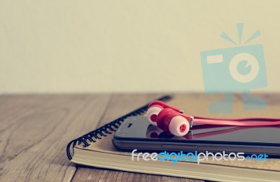 Earphones, Smart Phone And Notepad Are On Table Stock Photo