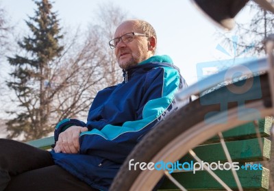 Eldely Man Sitting On A Bench Near His Bicycle In A City Park Stock Photo