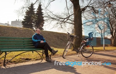 Elderly Man Sitting On A Bench Near His Bicycle In A City Park Stock Photo