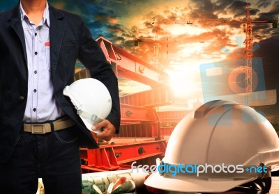 Engineer Man With White Safety Helmet Standing Against Working Table And Building Construction Scene Stock Photo