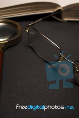 Eyeglasses With Magnifying Glass On Dark Surface With Books Stock Photo