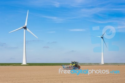 Farmer On Tractor Sowing In Soil Near Dike And Windmills Stock Photo