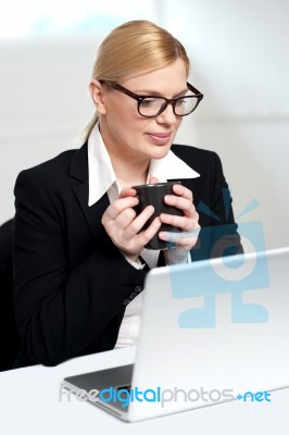 Female Executive Looking At Laptop Holding Mug Stock Photo