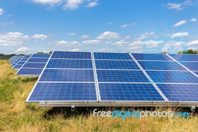 Field With Rows Of Blue Solar Collectors In Grass Stock Photo