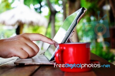 Finger Touching On Tablet With Red Cup On Table In Garden Stock Photo