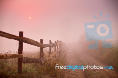 Foggy Rural Scene. Fence And Dirt Road At Misty Morning Stock Photo