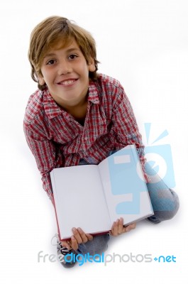 Front View Of Boy Sitting On Books And Reading Book Stock Photo