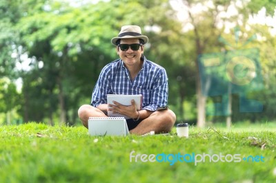 Full Length Of A Happy Smiling Mid Aged Man Sitting In Park Hold… Stock Photo