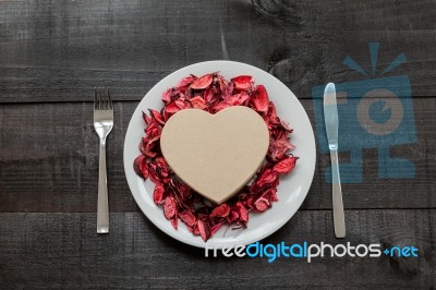 Gift, Plate And Cutlery Surrounded By Dry Petals On Wooden Stock Photo