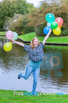 Girl Holding Up Many  Coloured Balloons At Pond Stock Photo