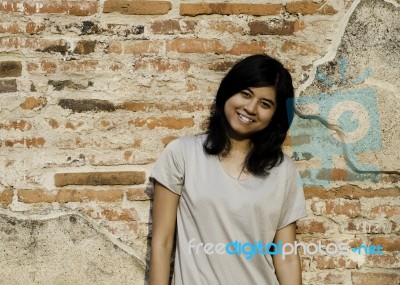 Girl Posing And Smiling While Standing Near Brick Wall Stock Photo