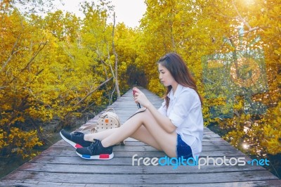 Girl Sitting Alone And Hand Holding Camera On A The Wooden Bridge In Autumn. Vintage Tone Stock Photo