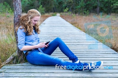 Girl Sitting On Wooden Path In Nature Phoning Mobile Stock Photo