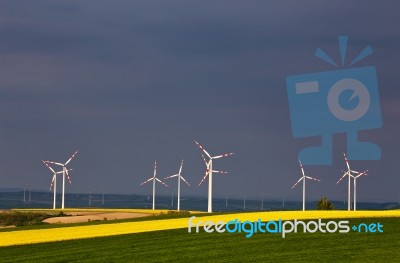 Green And Yellow Fields With Wind Turbines Generating Electricit… Stock Photo