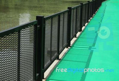 Green Walkway With Metal Fence By The Lake Stock Photo