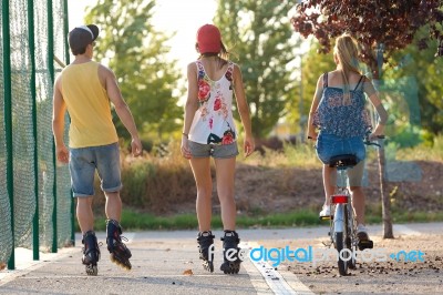 Group Of Friends With Roller Skates And Bike Riding In The Park Stock Photo