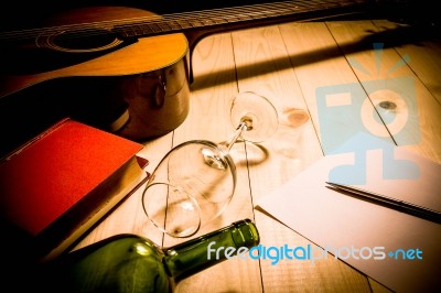 Guitar With Red Book And Wine On A Wooden Table Stock Photo