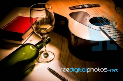 Guitar With Red Book And Wine On A Wooden Table Stock Photo