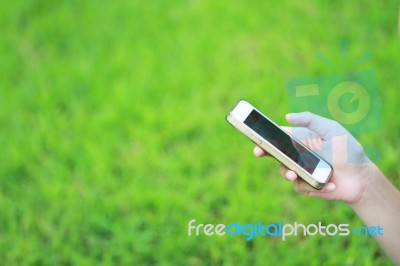 Hand Hold Smart Phone Against Green Grass Background Stock Photo