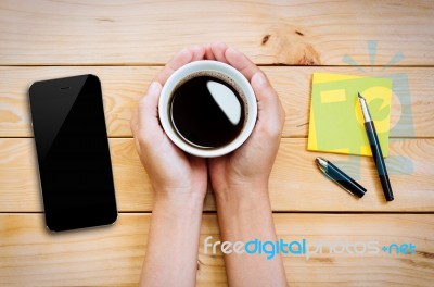 Hand Holding Coffee Cup With Smartphone And Notepad On Wood Stock Photo