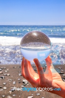 Hand Holding Glass Sphere At Beach And Sea Stock Photo